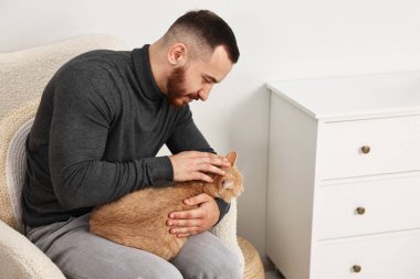 Evdeki koltukta sevimli kızıl kediyi okşayan adam.