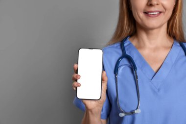 Doktor gri arka planda boş ekranlı akıllı telefonu gösteriyor, yakın plan. Tasarım için model