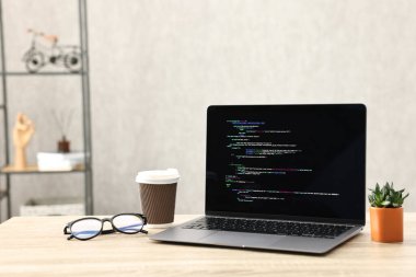 Programcının işyeri. Tamamlanmamış kodu olan modern bir bilgisayar, kağıt bardak, bardak ve ev bitkisi.