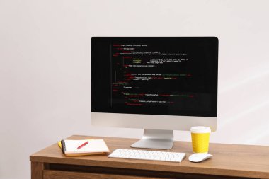 Programcının işyeri. Tamamlanmamış kodu olan modern bir bilgisayar, masa içinde bir bardak kağıt içki ve kırtasiye malzemesi.
