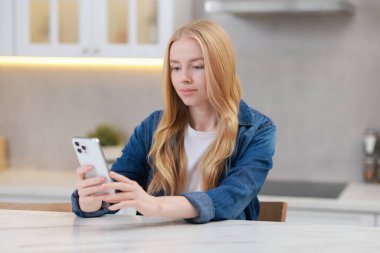 Mutfaktaki beyaz masada akıllı telefon kullanan güzel bir kadın.