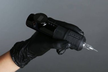 Profesyonel kozmetik uzmanı gri arka planda kalıcı makyaj makinesi tutuyor.