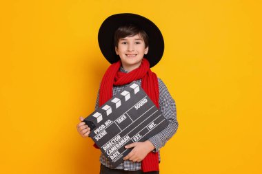 Turuncu arka planda film yönetmeni gibi davranan alkışlı çocuk. Geleceğin mesleğini hayal etmek