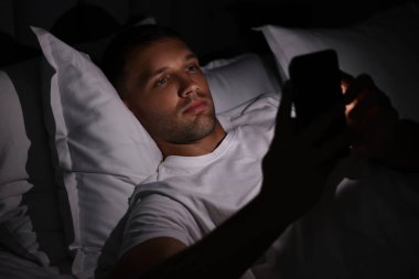 Kötü alışkanlık. Adam gece yatakta akıllı telefon kullanıyor.