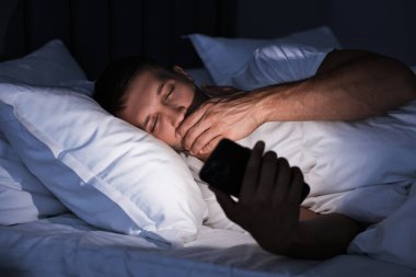 Kötü alışkanlık. Adam gece yatakta akıllı telefon kullanıyor.