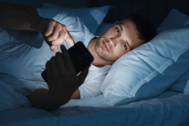 Kötü alışkanlık. Adam gece yatakta akıllı telefon kullanıyor.