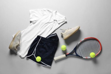 Tenis raketi, toplar, spor ayakkabısı ve gri arka planda spor giysisi, düz yatış