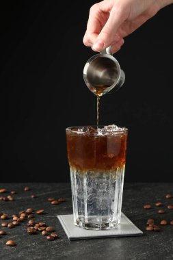 Karanlık masada ferahlatıcı espresso tonik yapan kadın, yakın plan.