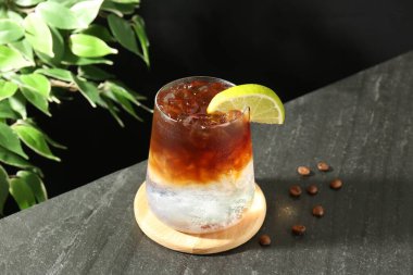 Koyu masada limon dilimi ve kahve çekirdeği ile espresso toniği tazeleniyor.