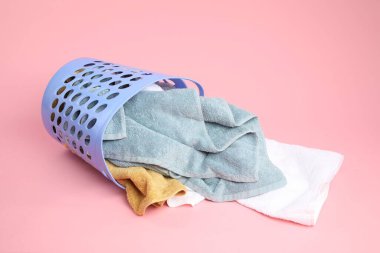 Pembe arka planda içi havlu dolu çamaşır sepeti devrilmiş.