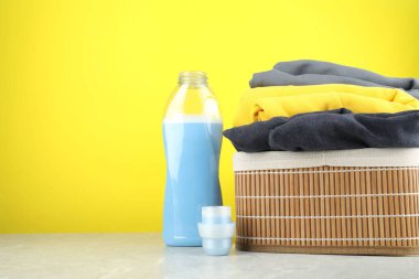 Şişe, kep ve giysi içinde çamaşır deterjanı gri mermer masa üzerinde sarı arka plan, metin için yer