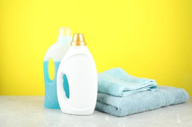 Çamaşır deterjanı şişelerde ve havlularda gri mermer masada sarı arka planda.