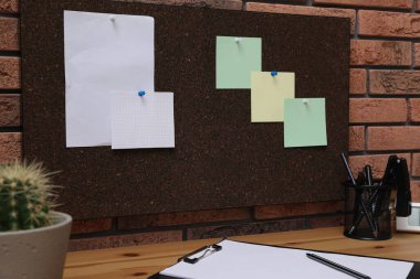 Ofisteki masanın üstündeki tuğladan duvara iğneli notlar asılmış mantar tahta.