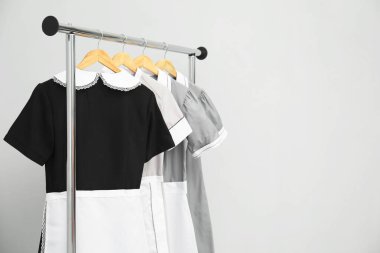 Maids' uniforms on clothing rack against grey background. Space for text clipart