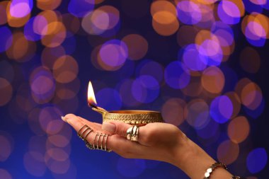 Diwali kutlaması. Renkli arka planda yanan diya lambasını tutan bulanık ışıklı kadın, yakın plan