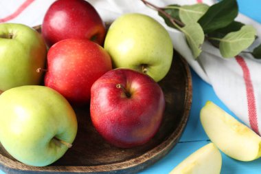 Açık mavi ahşap masada taze kırmızı ve yeşil elmalar, yakın plan.