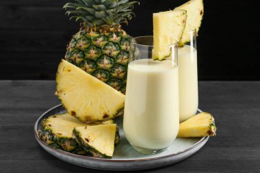 Bardakta lezzetli ananas püresi ve siyah ahşap masada meyve, yakın plan.