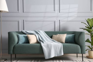 Gri duvarın yanında rahat bir kanepe, çiçek ve lamba.