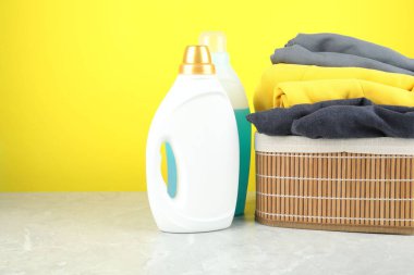 Şişelerde çamaşır deterjanı ve gri mermer masada giysiler sarı arka planda, metin için boşluk