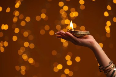 Diwali kutlaması. Kahverengi arka planda yanan diya lambası tutan bir kadın, yakın plan. Metin için boşluk
