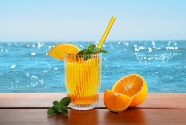 Plajdaki ahşap masada saman ve taze portakalla ferahlatıcı içecek.