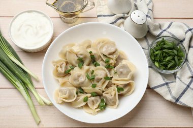 Beyaz ahşap masada servis edilen yeşil soğanlı leziz pelmeni.