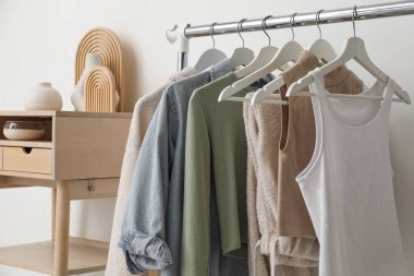 Giysilerle dizilin ve beyaz duvarın yanında ayakta durun.