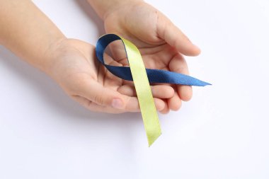 Beyaz arka planda sarı ve mavi kurdeleli çocuk, yakın plan. Down sendromu farkındalığı