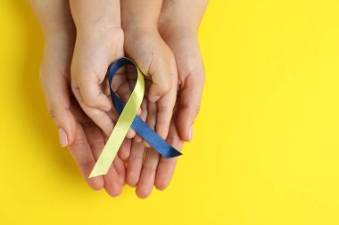 Arka planda sarı ve mavi kurdeleli çocuklu bir kadın. Down sendromu farkındalığı