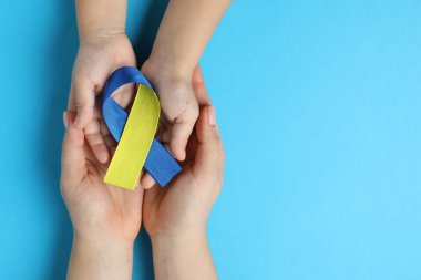 Çocuklu bir kadın elinde sarı ve mavi kurdeleler tutuyor. Arka planda, üst tarafta. Down sendromu farkındalığı