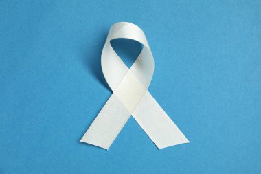 White awareness ribbon on blue background, top view