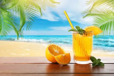 Plajdaki ahşap masada saman ve taze portakalla ferahlatıcı içecek.