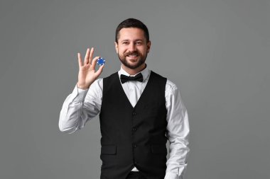 Gri arka planda kumarhane fişi olan krupiye.