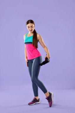 Açık mor arka planda kalça kaslarını gevşetmek için perküsyon masaj aleti kullanan kadın.