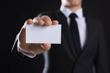 Siyah arka planda boş bir kartvizit tutan adam, yakın plan. Tasarım için model