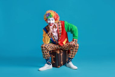 Mavi arka planda bavulda oturan mutlu palyaço.