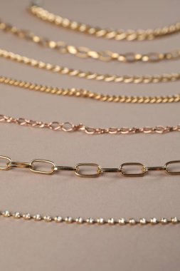 Açık kahverengi arka planda farklı metal zincirler, yakın plan. Lüks mücevherler.