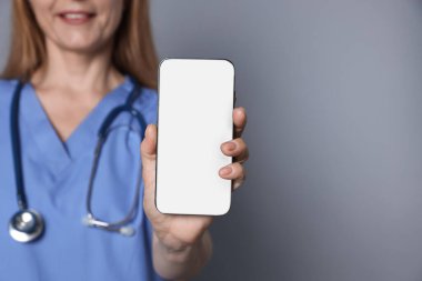 Doktor gri arka planda boş ekranlı akıllı telefonu gösteriyor, yakın plan. Tasarım için model