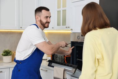 Gülümseyen tamirci mutfakta fırının yanındaki kadına danışıyor.