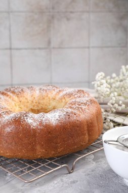 Gri masadaki pudra şekerli ve çiçekli taze pişmiş sünger keki, yakın plan.