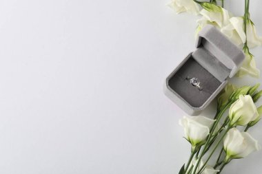 Güzel bir yüzük, kutuda değerli taşlar ve beyaz arka planda çiçekler, manzaranın üstünde. Metin için boşluk