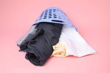 Pembe arka planda içi kıyafet dolu çamaşır sepeti devrilmiş.