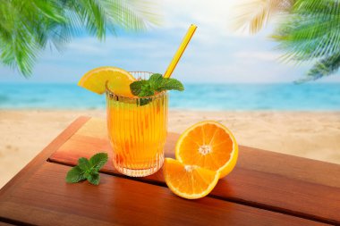 Plajdaki ahşap masada saman ve taze portakalla ferahlatıcı içecek.