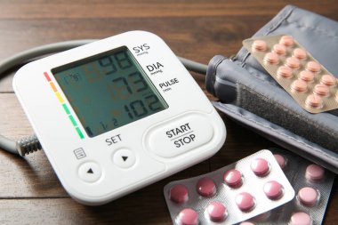 Kan basıncı ölçme cihazı ve tahta masada haplar, yakın plan.