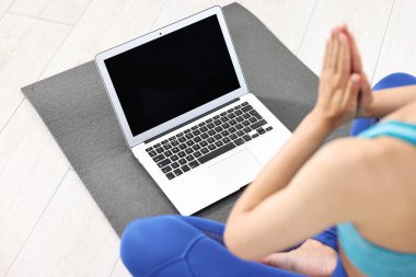 Evde yoga minderinde dizüstü bilgisayar başında meditasyon yapan bir kadın.
