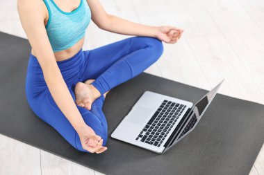 Evde yoga minderinde dizüstü bilgisayar başında meditasyon yapan bir kadın.