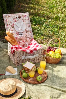 Masa takımlı piknik sepeti, farklı atıştırmalıklar, meyve suyu ve şapka.