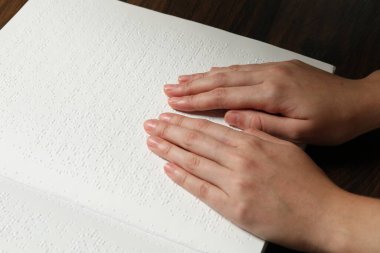 Kör kadın körler alfabesiyle yazılmış bir kitap okuyor. Ahşap masada, yakın plan.