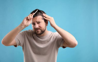 Adam açık mavi arka planda saçını tarıyor, mesaj için yer var. Alopecia sorunu