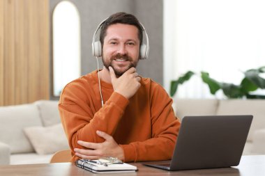 Interpreter in headphones having video chat via laptop at wooden table indoors clipart